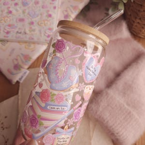 May include: A clear glass tumbler with a bamboo lid and a glass straw. The tumbler is decorated with ice skates, roses, and the text "Love on Ice" and "Smells Like Hockey Romance". The design is in pastel colors.