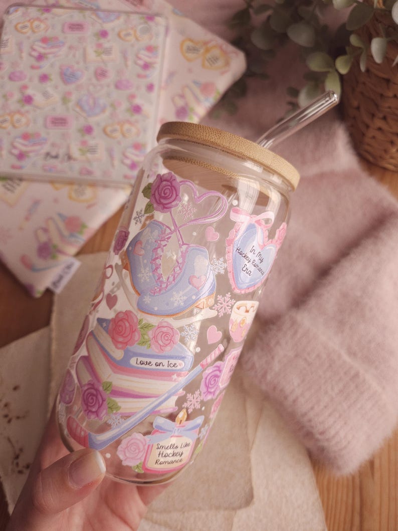 May include: A clear glass tumbler with a bamboo lid and a glass straw. The tumbler is decorated with ice skates, roses, and the text "Love on Ice" and "Smells Like Hockey Romance". The design is in pastel colors.