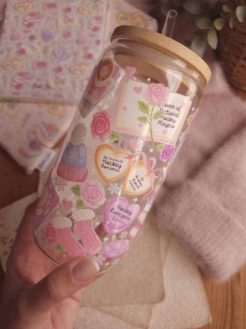 May include: A clear glass tumbler with a bamboo lid and straw, decorated with pink and white stickers. The stickers feature roses, hearts, and text that reads "Hockey Romance Girlie" and "Lover of Fictional Hockey Players."