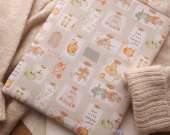 Puede incluir: Una funda de libro de tela beige con un patrón repetido de calabazas, frascos e ilustraciones de temática otoñal. El texto "Down the pumpkin patch" se repite en la cubierta.