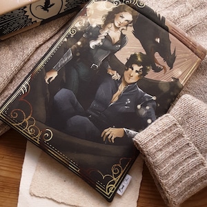 Può includere: Una copertina di un libro con un'illustrazione fantasy di due persone con un drago sullo sfondo. La copertina è dorata e nera con dettagli decorativi. Il testo sulla copertina recita "Born of Chaos".