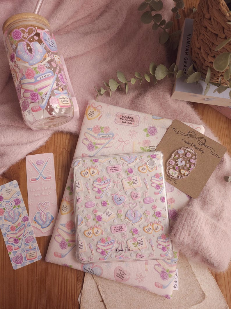 May include: A collection of pink and white stationery and accessories, including a tumbler, tablet case, stickers, and a phone grip. The items feature a repeating pattern of books, roses, and ice skates. The text "Hockey Romance Book Club" is visible.