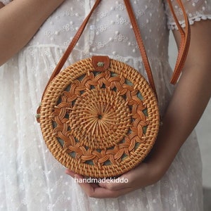 May include: A round, woven, brown rattan bag with a leather strap. The bag has a circular design with a woven pattern.