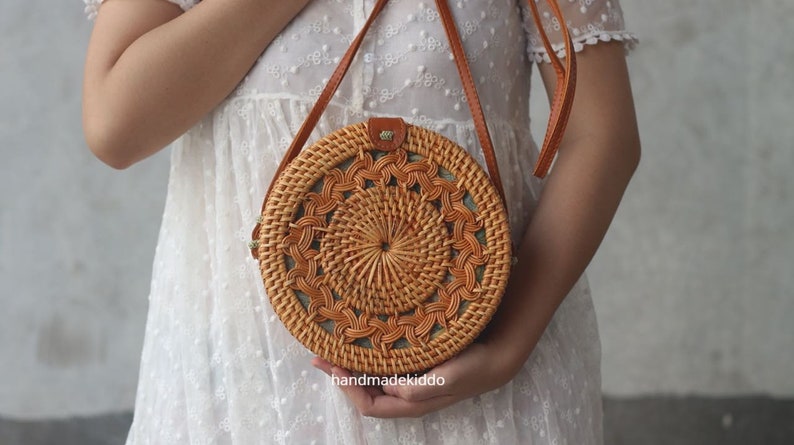 May include: A round, woven, brown rattan bag with a leather strap. The bag has a circular design with a woven pattern.