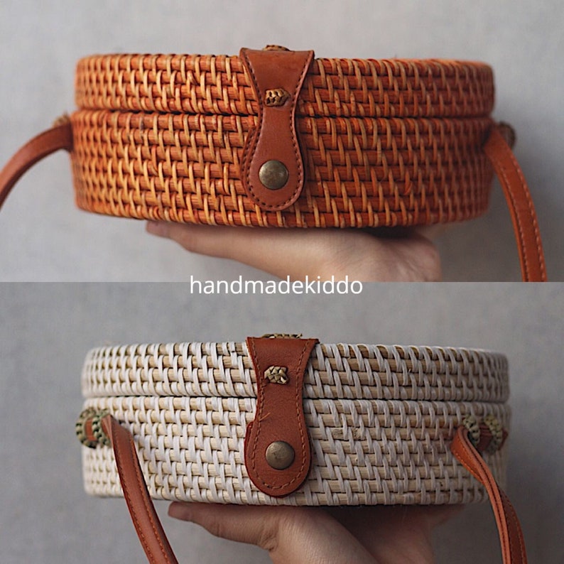 May include: Two round woven rattan bags with brown leather straps and gold accents. The top bag is brown and the bottom bag is white.