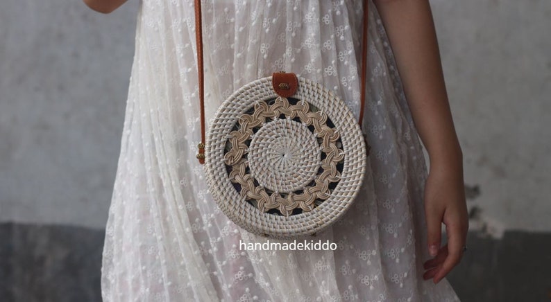 May include: White round woven rattan bag with a brown leather strap. The bag has a circular pattern with a woven design.