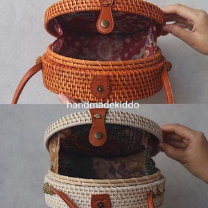 May include: Two round woven rattan bags with leather straps and closures. The top bag is brown and the bottom bag is white.
