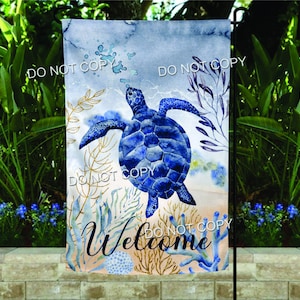 May include: A watercolor garden flag with a blue sea turtle swimming in the ocean. The flag has a light blue background with white and gold accents. The text "Welcome" is written in a cursive font on the bottom of the flag.