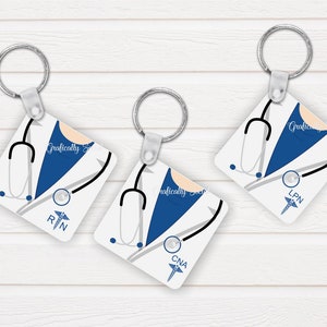 May include: Three white square keychains with blue accents and a stethoscope design. Each keychain has a different medical abbreviation: RN, LPN, and CNA.