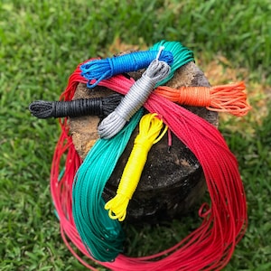 May include: Assortment of colourful ropes in red, green, blue, black, silver, and yellow, coiled and stacked on a wooden stump.