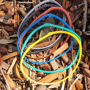 May include: A set of six colorful rope rings, arranged in a rainbow pattern, with the yellow ring on the bottom and the gray ring on top. The rings are lying on a bed of brown wood chips.