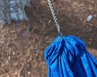 May include: Close-up of a blue hammock with a gray rope attached to it. The hammock is folded and bundled together.