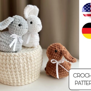 Op de afbeelding: Haakpatroon voor drie amigurumi konijnen speelgoed. De konijnen zijn grijs, wit en bruin. Het patroon bevat instructies voor het maken van de konijnen en een mand.