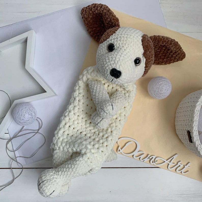 Peut inclure: Un jouet en crochet blanc en forme de chien avec des oreilles brunes. Le jouet est pos&eacute; sur une surface brun clair avec un objet blanc en forme d'&eacute;toile et une boule blanche.