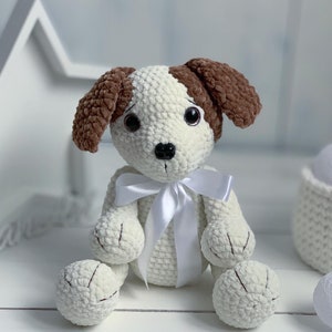 Peut inclure: Un jouet en crochet pour chien blanc avec des oreilles brunes et un ruban de satin blanc. Le chien a des yeux noirs et un nez noir.