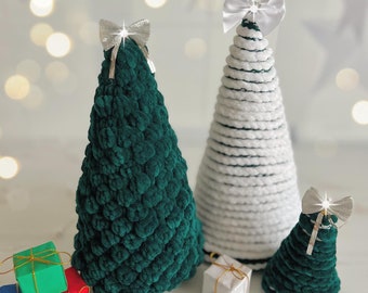 Könnte beinhalten: Eine Sammlung handgefertigter Weihnachtsbaumdekorationen. Das Set umfasst zwei grüne und einen weißen gehäkelten Baum, jeder mit einer silbernen oder weißen Schleife. Kleine Geschenkboxen in verschiedenen Farben sind am Boden angeordnet, was eine festliche Szene schafft.