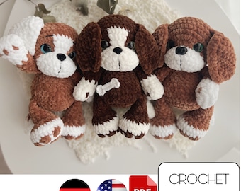 May include: Three brown crocheted plush dog toys with white accents. The dogs have brown fur, white faces, and white paws. The dogs are sitting on a white surface. The image includes the text "CROCHET PATTERN" in red letters.