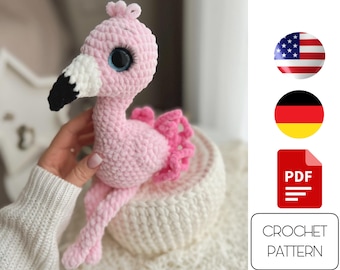 May include: Pink crocheted flamingo amigurumi toy with white and black details. The toy is sitting on a white crocheted surface. Crochet pattern PDF included.