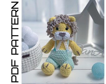 May include: A crocheted lion toy with a yellow body, gray mane, and blue overalls. The lion is sitting on a white surface with a white basket and a blue ball.