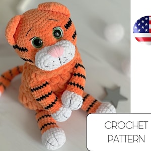 Puede incluir: Patrón de crochet para un adorable juguete amigurumi de tigre rayado naranja y negro. El juguete tiene patas blancas y una nariz rosa.