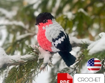 May include: Crochet pattern for a red and black bird with white accents. The bird is sitting on a snowy pine branch. The pattern is available as a PDF download. The image also includes a US flag.