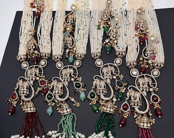 May include: Several beaded necklaces with intricate pendants. The necklaces feature multiple strands of white beads, with pendants showcasing elephant designs, gemstones, and dangling tassels in various colors like red, green, and pink. The jewelry has a gold-tone finish.