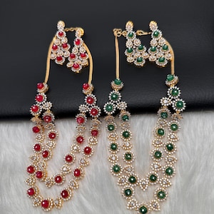 May include: Two sets of gold-toned jewelry, each including a necklace and matching earrings. One set features red gemstones, the other green. Both sets have a floral design with clear accent stones.