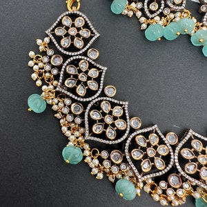 May include: An ornate necklace and earring set. The necklace features a floral design with clear stones set in a black and silver frame, accented with small pearls and light green beads. The earrings have a large oval green stone.