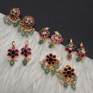May include: A collection of gold-toned earrings featuring floral and paisley motifs. The jewelry is adorned with vibrant pink and deep green stones, accented by small white pearls and dangling light green beads, creating a detailed set of accessories.