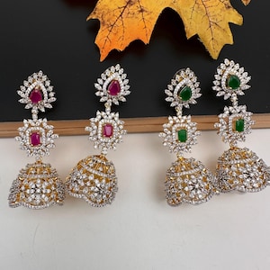 May include: Four pairs of gold-toned, ornate earrings with clear and colored gemstones. Each earring features a teardrop-shaped gem at the top, a square gem in the middle, and a bell-shaped bottom. The gemstones are red and green.