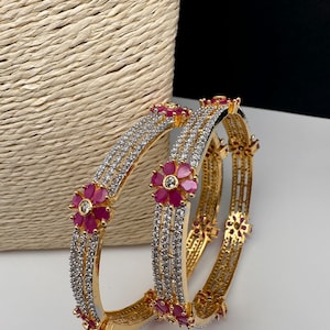 Peut inclure: Bracelets dorés avec des détails complexes. Chaque bracelet est orné de rangées de pierres scintillantes et de fleurs rouges. Le design est élégant et accrocheur, idéal pour les occasions spéciales.