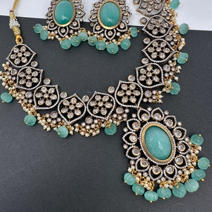 May include: An ornate jewelry set featuring a necklace and matching earrings. The set includes a necklace with a large oval pendant and a pair of earrings, each with a large oval stone. The jewelry is embellished with small white stones and light green beads.