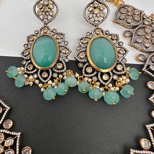 May include: Close-up of an ornate jewelry set featuring earrings and a necklace. The earrings have large oval, light green stones, surrounded by gold and silver filigree, and dangling green beads. The necklace has a similar design.