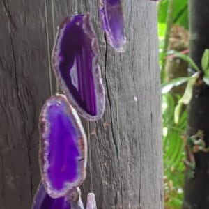 May include: Purple agate wind chime with seven pieces of agate hanging from a string. The agate is translucent and has a white and purple pattern.