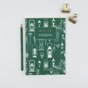 May include: A green journal with a white pattern of lanterns and light bulbs. The text "WRITE Wisdom" is printed in copper on the front cover.