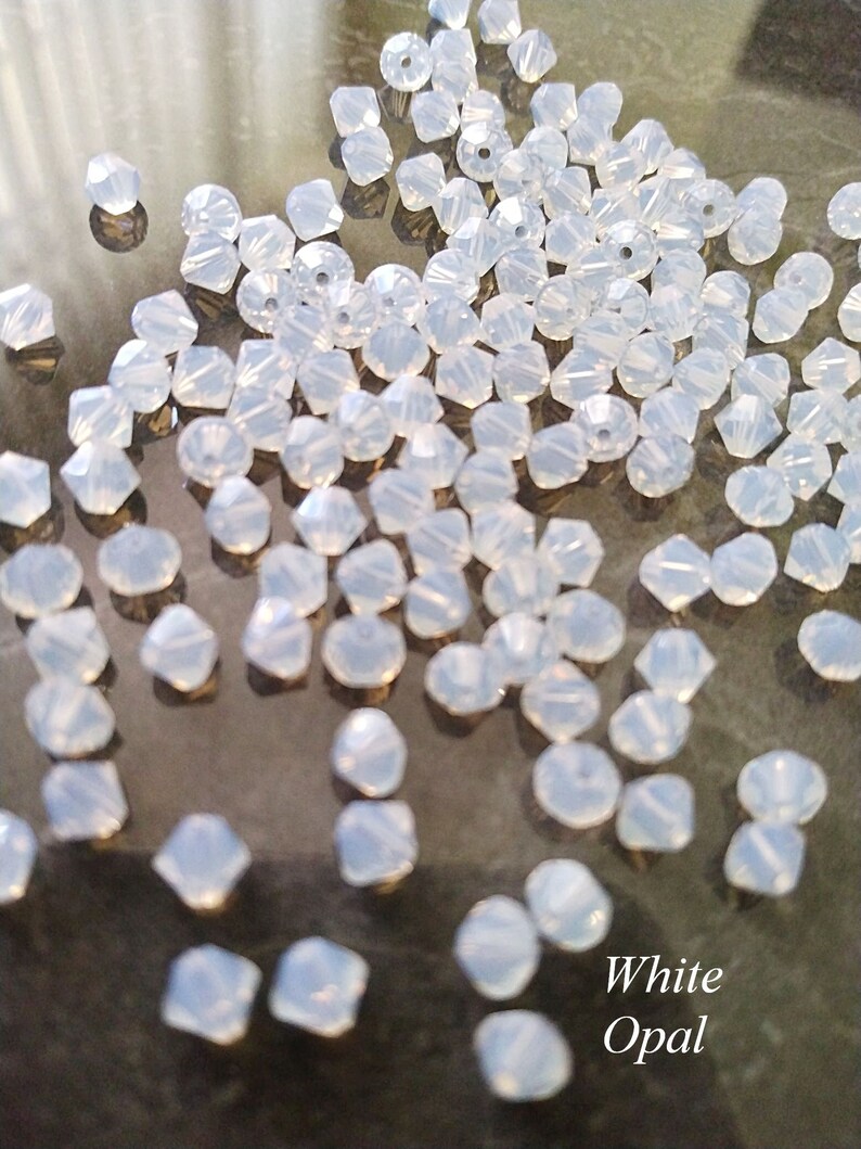 May include: A large quantity of white opal bicone beads. The beads are faceted and have a pearlescent finish.