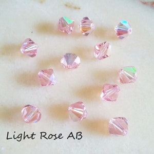 May include: A collection of 12 light rose AB crystal beads. The beads are faceted and have a light pink color with an iridescent finish.
