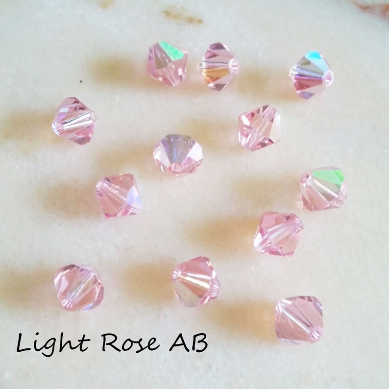 May include: A collection of 12 light rose AB crystal beads. The beads are faceted and have a light pink color with an iridescent finish.
