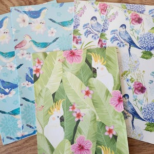 May include: A collection of four rectangular paper sheets featuring diverse bird and floral patterns. One sheet displays blue birds on a light blue background, another shows blue birds with blue hydrangeas, and one features white cockatoos.