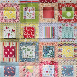 Puede incluir: Una colcha de retazos con una variedad de patrones coloridos, que incluyen lunares, rayas y diseños florales. La colcha está hecha de cuadrados individuales que se cosen juntos para crear un diseño más grande.