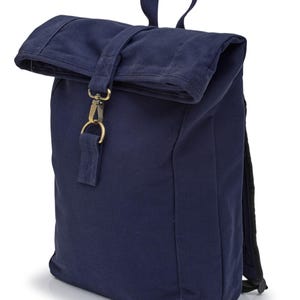 May include: A navy blue roll-top backpack featuring a fabric strap closure with a brass-toned metal lobster clasp and D-ring. The bag includes a top carry handle and adjustable shoulder straps, constructed from a durable, solid-colored textile material.