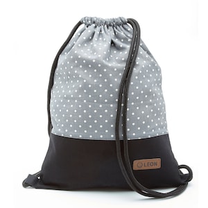 May include: A gray and black drawstring bag with white polka dots. The bag has a black drawstring and a brown leather patch with the word "LEON" on it.