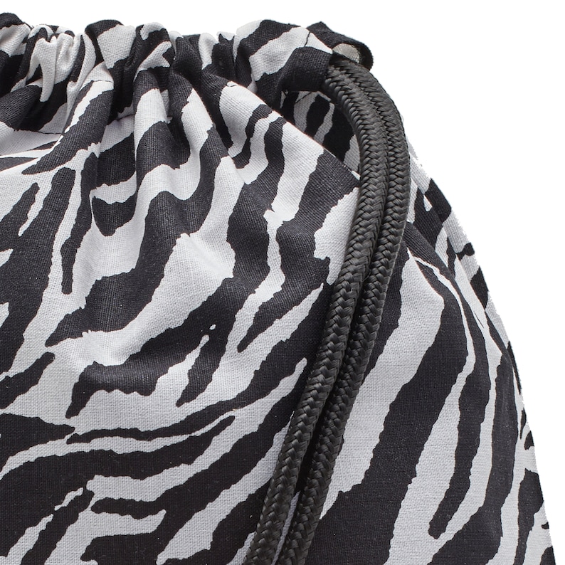 Op de afbeelding: Close-up van een zwart-witte zebraprint trekkoordtas met zwarte trekkoorden.