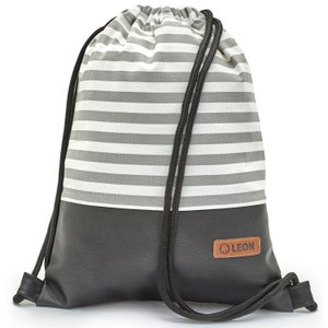 Può includere: Una borsa a cordoncino a righe grigie e bianche con un fondo in similpelle nero. La borsa ha un cordoncino nero e una toppa in pelle marrone con la scritta "LEON" su di essa.