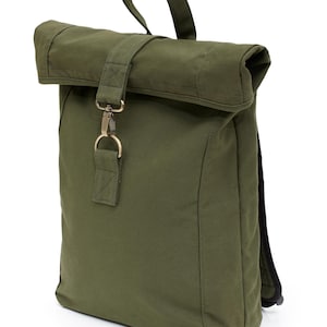 May include: An olive green roll-top backpack constructed from a durable fabric. The bag features a top handle, a central vertical strap with a metallic lobster clasp closure, and a rectangular main compartment with a folded top opening design.