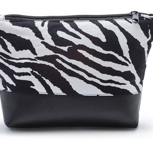 Op de afbeelding: Een zwarte en witte zebraprint ritsvak met een zwarte leren bodem.