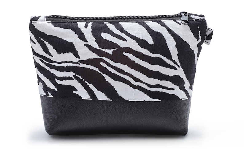 Op de afbeelding: Een zwarte en witte zebraprint ritsvak met een zwarte leren bodem.