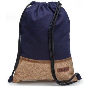 May include: A navy blue drawstring backpack with a cork bottom and a zippered pocket. The backpack has a black drawstring and a brown leather patch with the word "LEON" on it.
