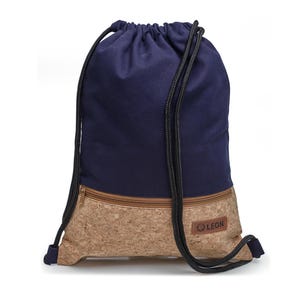 Op de afbeelding: Een marineblauwe rugzak met trekkoorden en een beige kurken onderpaneel met een horizontale ritszak. De tas heeft zwarte gevlochten koordhengsels en een rechthoekige bruine patch in de rechterbenedenhoek met de tekst LEON erop gedrukt.