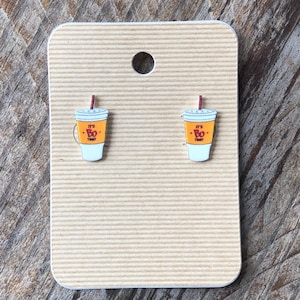May include: A pair of earrings featuring a white cup with a red straw and the text "It's Bo Time" in orange and red. The earrings are displayed on a brown card.
